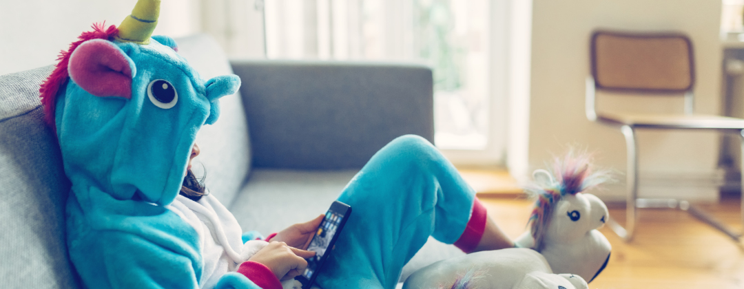 little girl in unicorn costume with mobile on couch